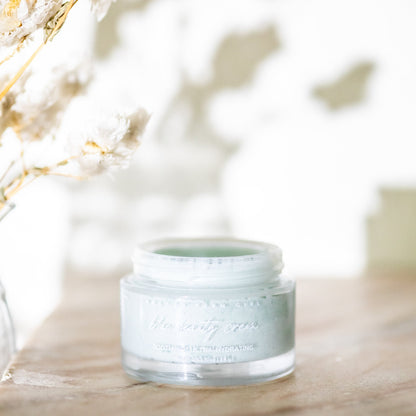 Blue Beauty Cream Soothing Tallow Face Cream in a clear jar on a wooden surface with dried flowers in the background.