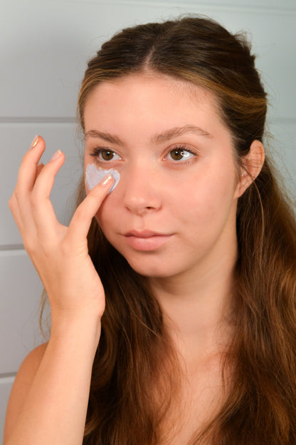A woman applies Blue Beauty Cream Soothing Tallow Face Cream to her cheek, showcasing its smooth texture and soothing propert