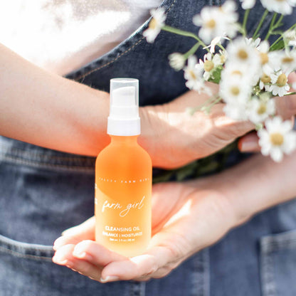 Dark Spot Brightening Kit featuring a bottle of cleansing oil held in hands, surrounded by flowers, showcasing a natural aest