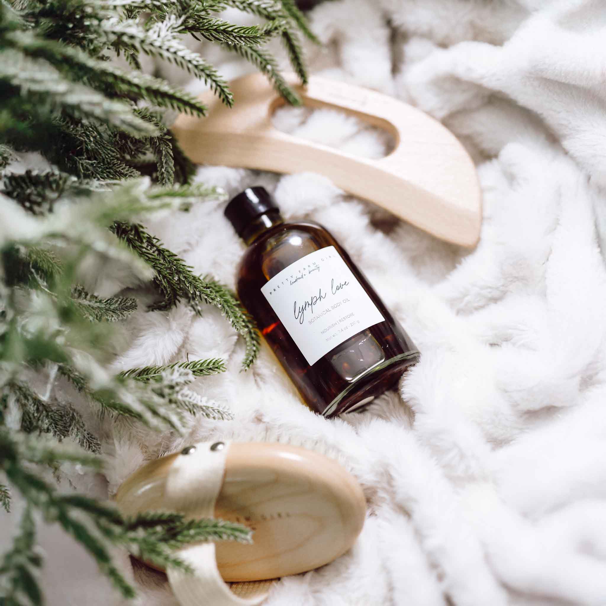 Body Care Lymphatic Routine Kit featuring a bottle of lymphatic oil, a wooden gua sha tool, and a brush on a soft blanket.