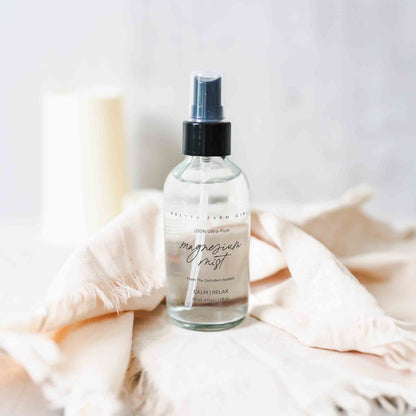 Magnesium Mist Body Spray in a clear bottle with a black spray top, placed on a soft, neutral fabric background.