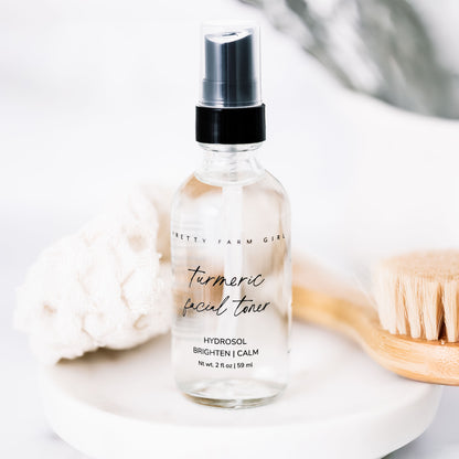 Dark Spot Brightening Kit featuring a turmeric facial toner in a clear spray bottle, with a wooden brush and soft cloth in th