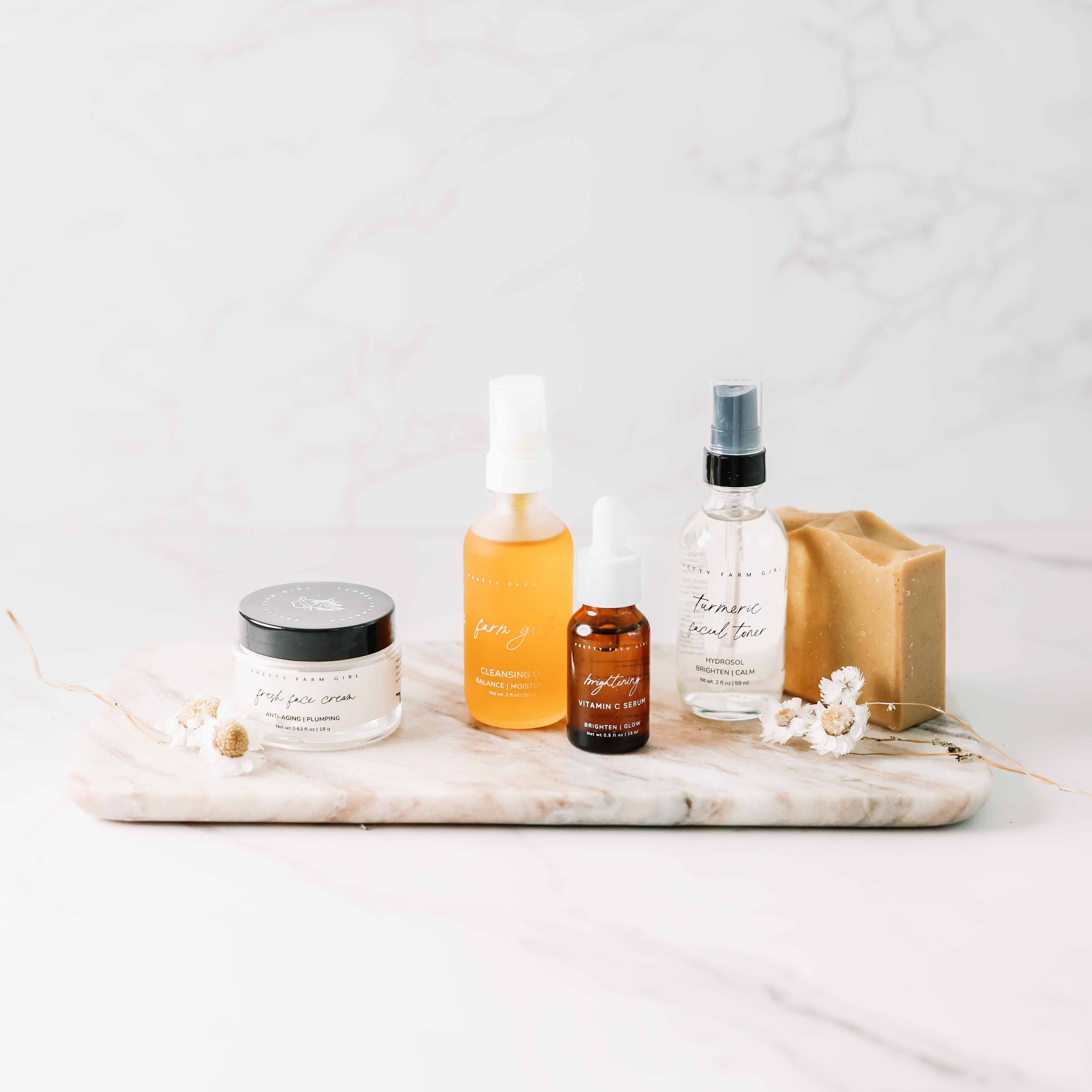 Dark Spot Brightening Kit featuring a cleanser, serum, moisturizer, and soap on a marble tray with floral accents.