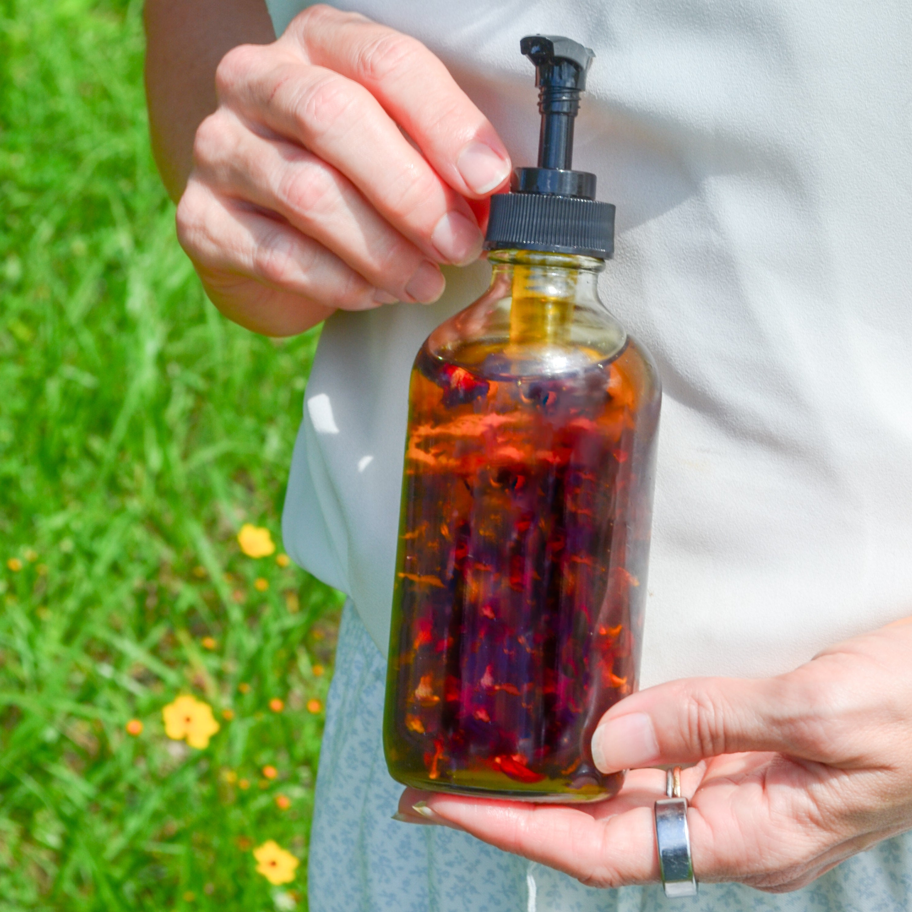 Body Care Lymphatic Routine Kit featuring a glass pump bottle filled with herbal infusion, held by a person outdoors.